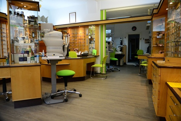 Modernes Optikergeschäft mit Brillenauswahl, Sehtestgeräten und grünen Stühlen.