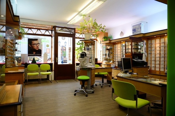 Modernes Optikergeschäft mit vielen Brillen, Beratungstischen und grünen Stühlen.